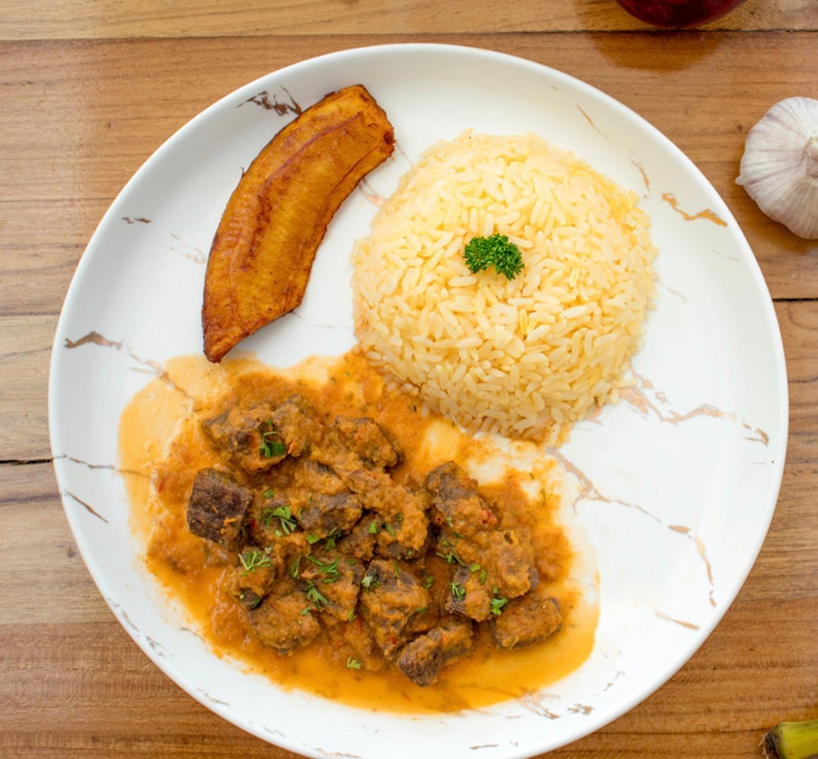 Delicious plate of rice, beef stew, and fried plantain garnished with parsley on a marble-patterned plate.